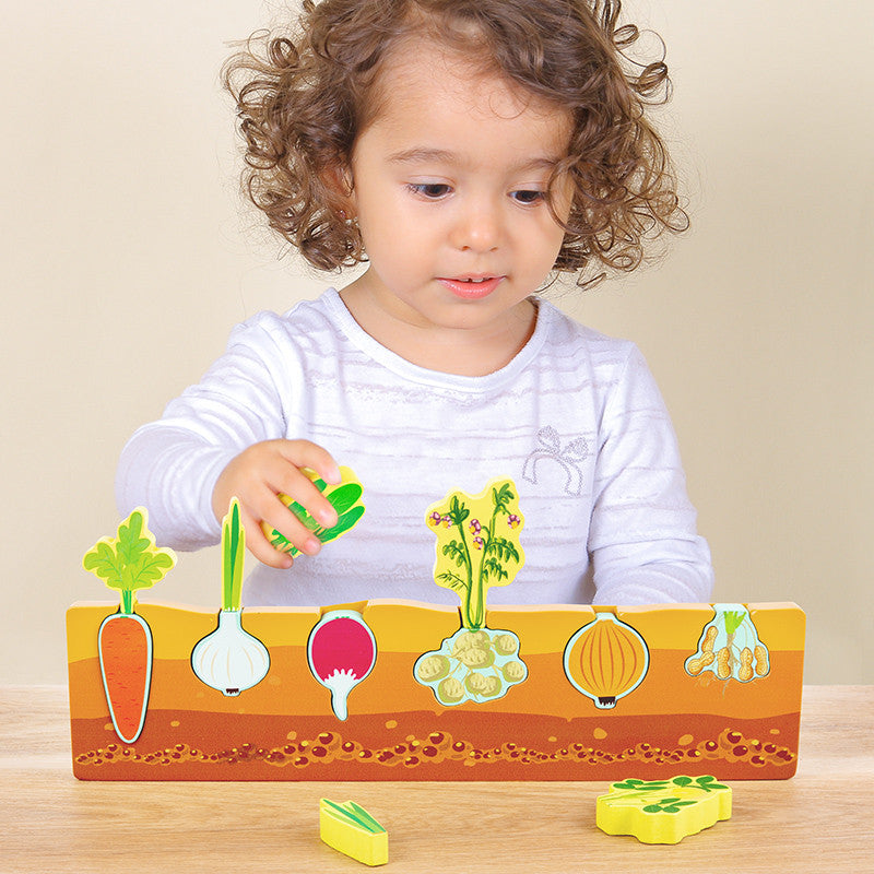 Gyermek játszik a Montessori zöldség puzzle-lel, kihúzza a répát és a fokhagymát.